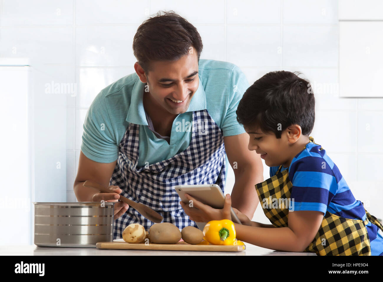 Vater und Sohn in Küche tragen Schürzen Blick auf digital-Tablette Stockfoto