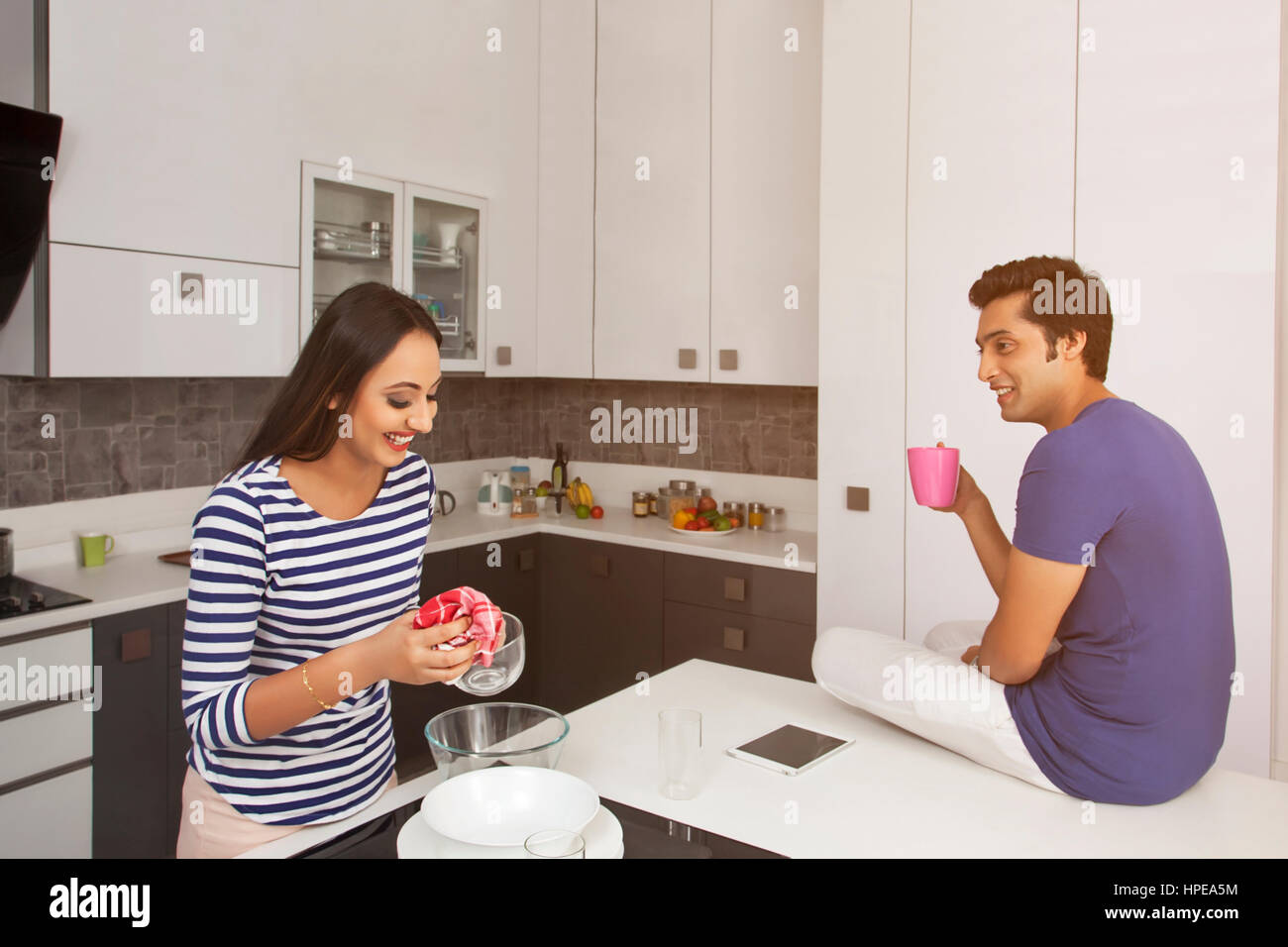 Frau, Reinigung Utensil in der Küche, während Ehemann Kaffeetrinken Stockfoto