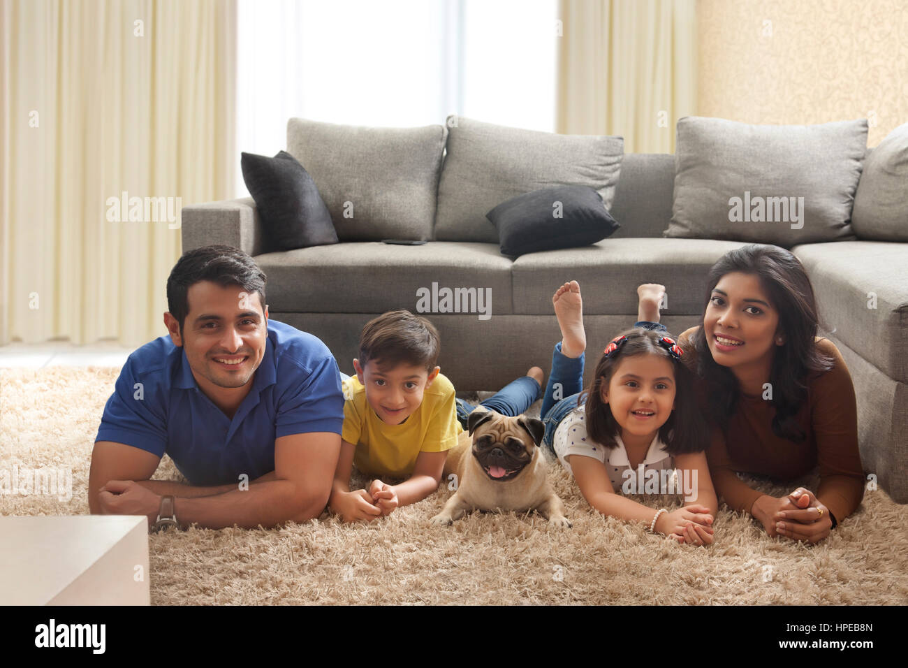 Glückliche Familie mit Mops posiert auf Teppich im Wohnzimmer Stockfoto