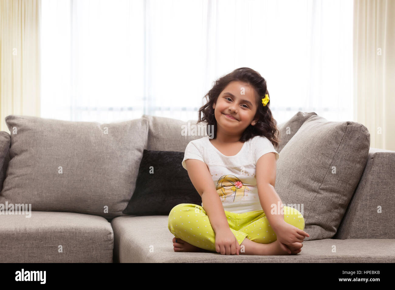 Lächelndes Mädchen sitzt im Schneidersitz auf sofa Stockfoto