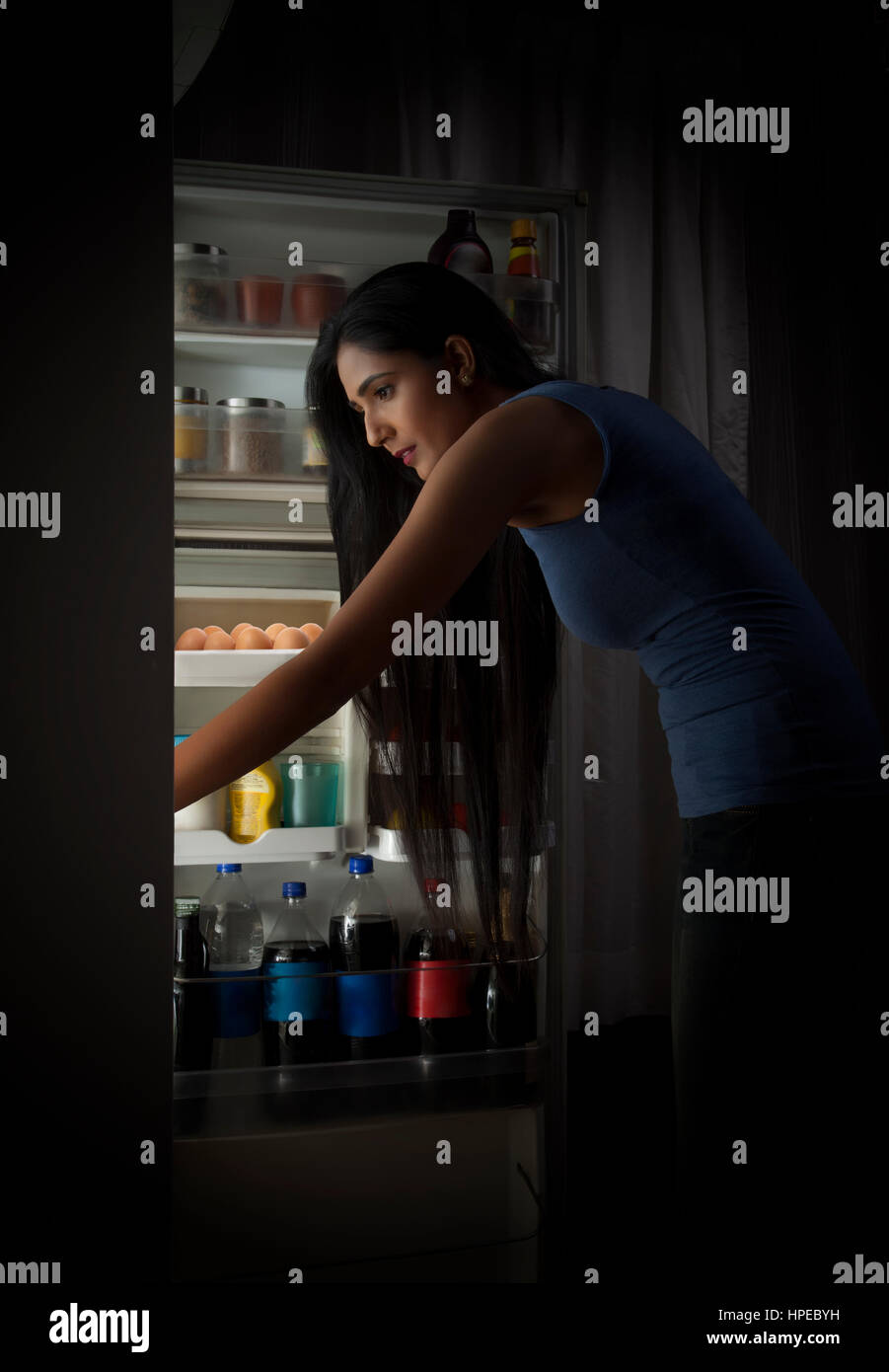 Junge Frau Suche Lebensmittel im Kühlschrank in der Nacht Stockfoto