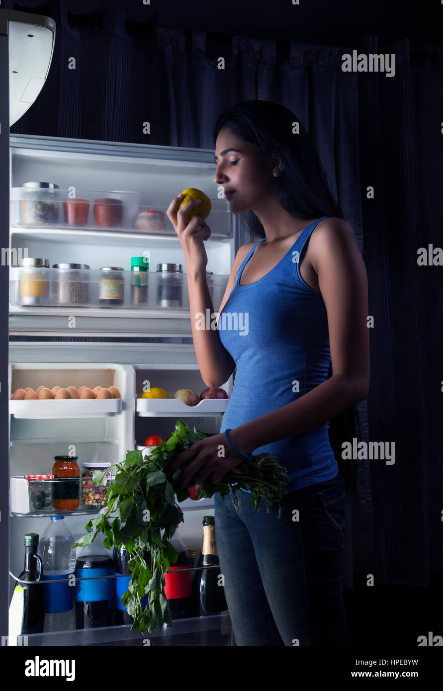 Junge Frau, die Einnahme von Obst und Blattgemüse aus Kühlschrank Stockfoto
