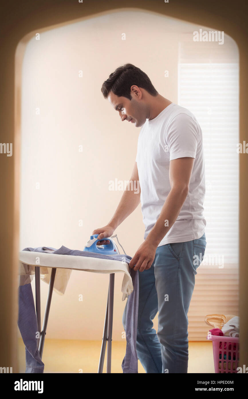 Junger Mann, ein Bügeleisen/-Brett sein Hemd im Zimmer Stockfoto