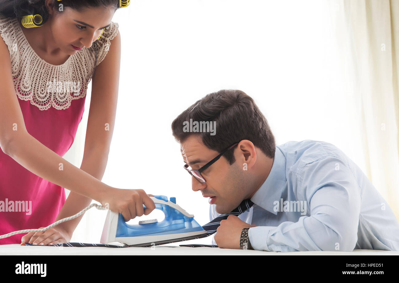 Junge Frau mit Lockenwickler Mannes Krawatte Bügeln Stockfoto