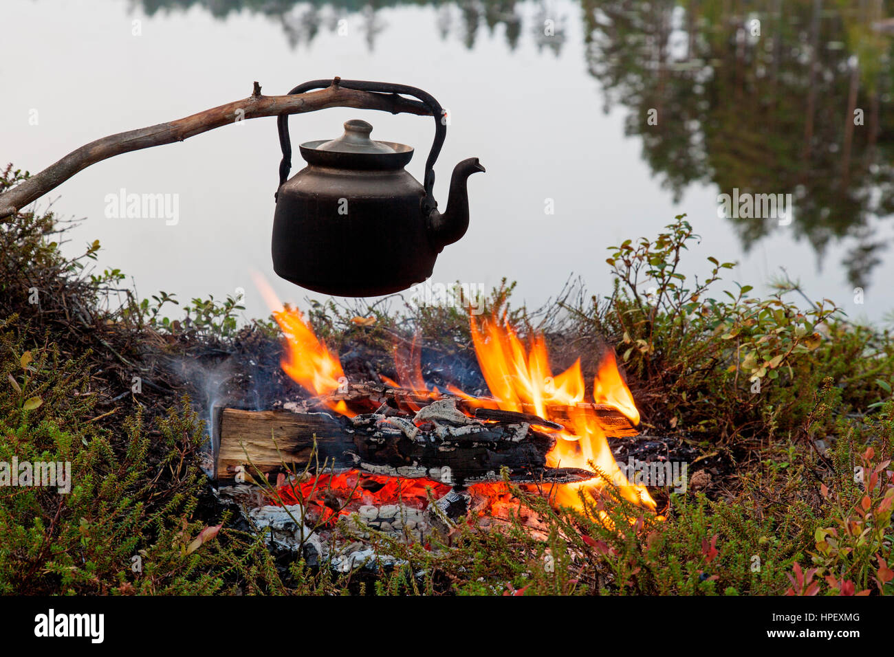 Geschwärzte Zinn Wasserkocher kochendes Wasser über Flammen von Lagerfeuer während der Wanderung entlang See Stockfoto