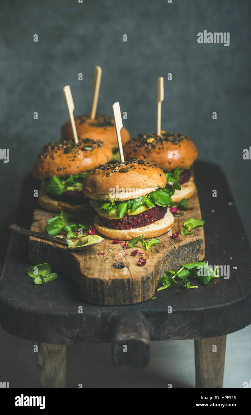 Gesunde vegane Burger mit rote Beete und Quinoa Patty, Rucola, Avocado-Sauce, Vollkorn Brötchen auf rustikalem Holzbrett über dunklen Holztisch, selektive Stockfoto