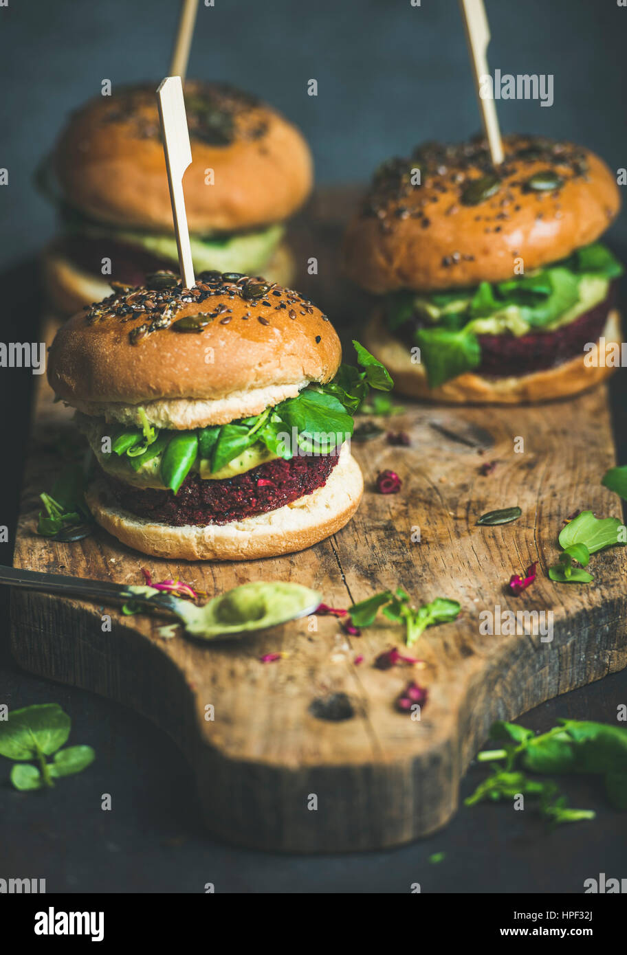 Gesunde vegane Burger mit rote Beete und Quinoa Patty, Rucola, Avocado-Sauce, Vollkorn Brötchen auf rustikalem Holzbrett auf dunklem Hintergrund, selektive fo Stockfoto