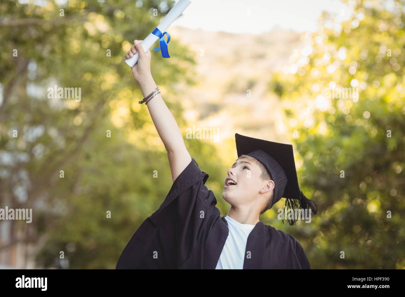 Aufgeregt graduate Schuljunge mit Grad Schriftrolle auf dem Campus in der Schule Stockfoto