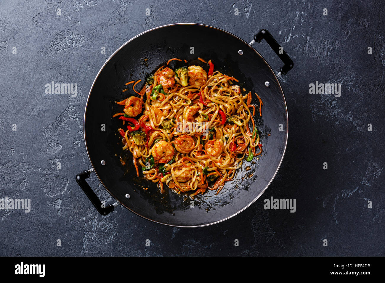 Stir-Fry Udon-Nudeln mit Garnelen in Wok-Pfanne auf dunklen Stein Hintergrund Stockfoto