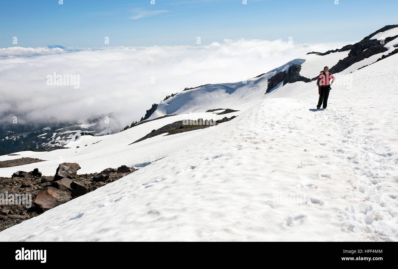 Eine weibliche Wanderer Abenteuer über den Wolken auf einem verschneiten Berg. Aufgenommen am Mount Rainer National Park im US-Bundesstaat Washington. Stockfoto