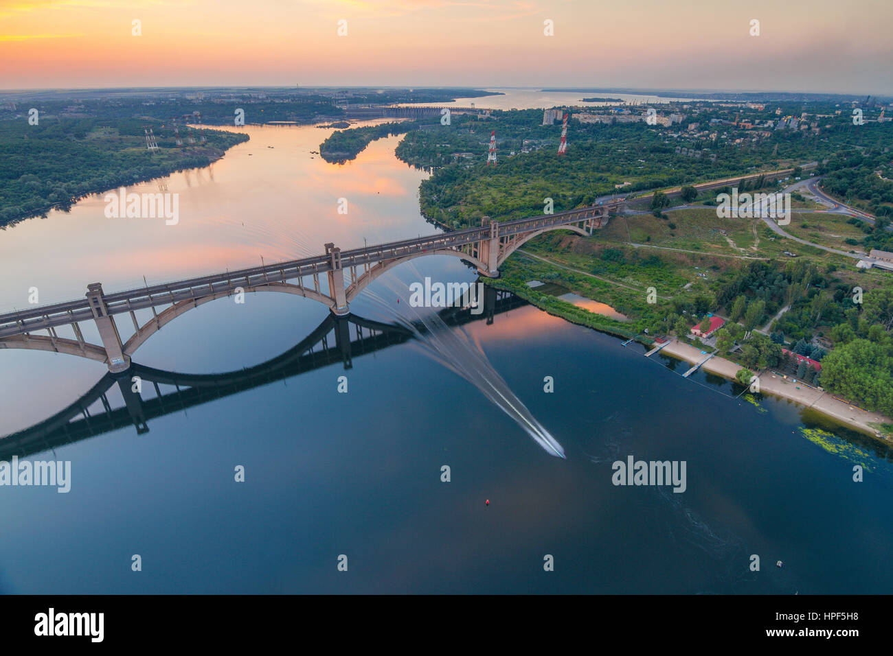 Abends auf Dnjepr und Preobraschenskij gewölbte Brücke aus einer Höhe von 180m mit Motorboot im Wasser, Zaporozhye, Ukraine Stockfoto