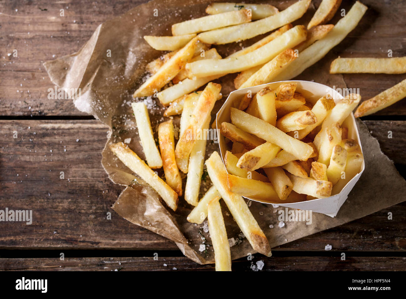 Fastfood Pommes frites Kartoffeln mit Haut mit Salz und Kräutern in Lunchpaket auf Backpapier über alten dunklen hölzernen Hintergrund serviert. Ansicht von oben Platz für Stockfoto