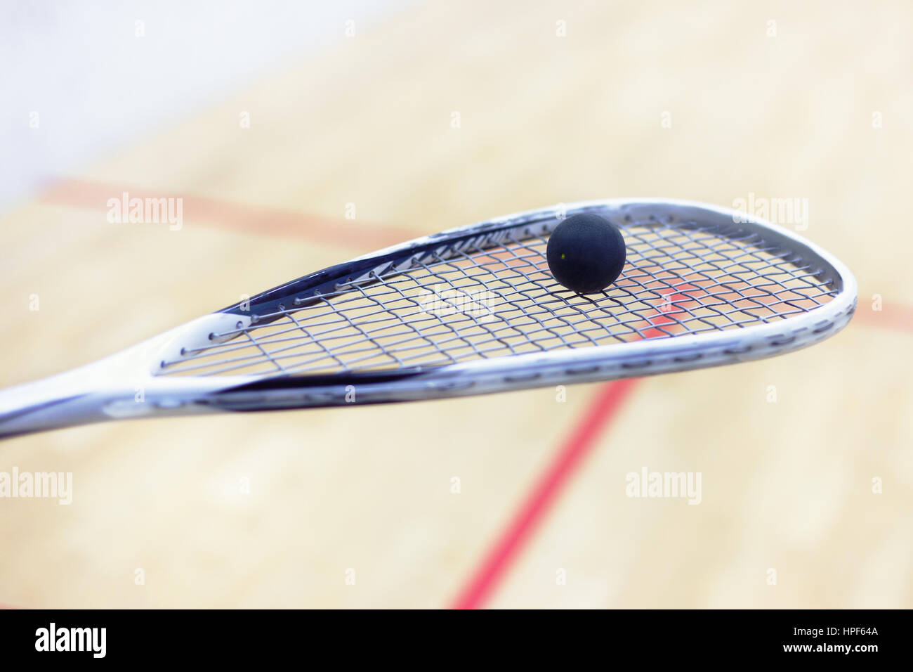 Squash-Schläger und Ball. Squash-Ausrüstung. Squash-Ball auf Squash-Schläger mit Gericht auf dem Hintergrund. Foto mit Muskelaufbau und selektiven Fokus Stockfoto