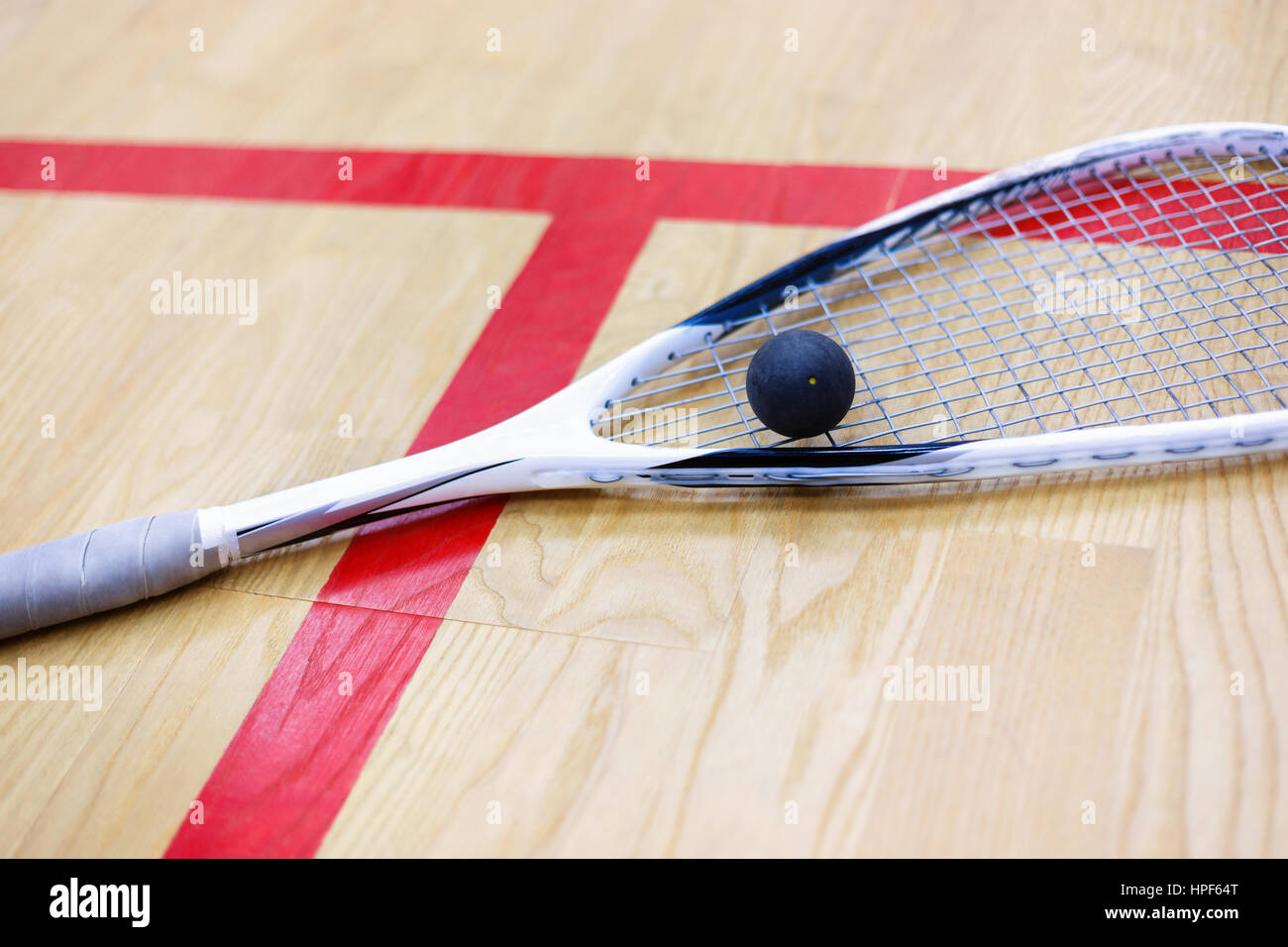 Squash-Schläger und Ball auf dem hölzernen Hintergrund. Squash-Ausrüstung. Squash-Ball und Squash Schläger auf dem Platz neben einer roten Linie. Foto mit sele Stockfoto