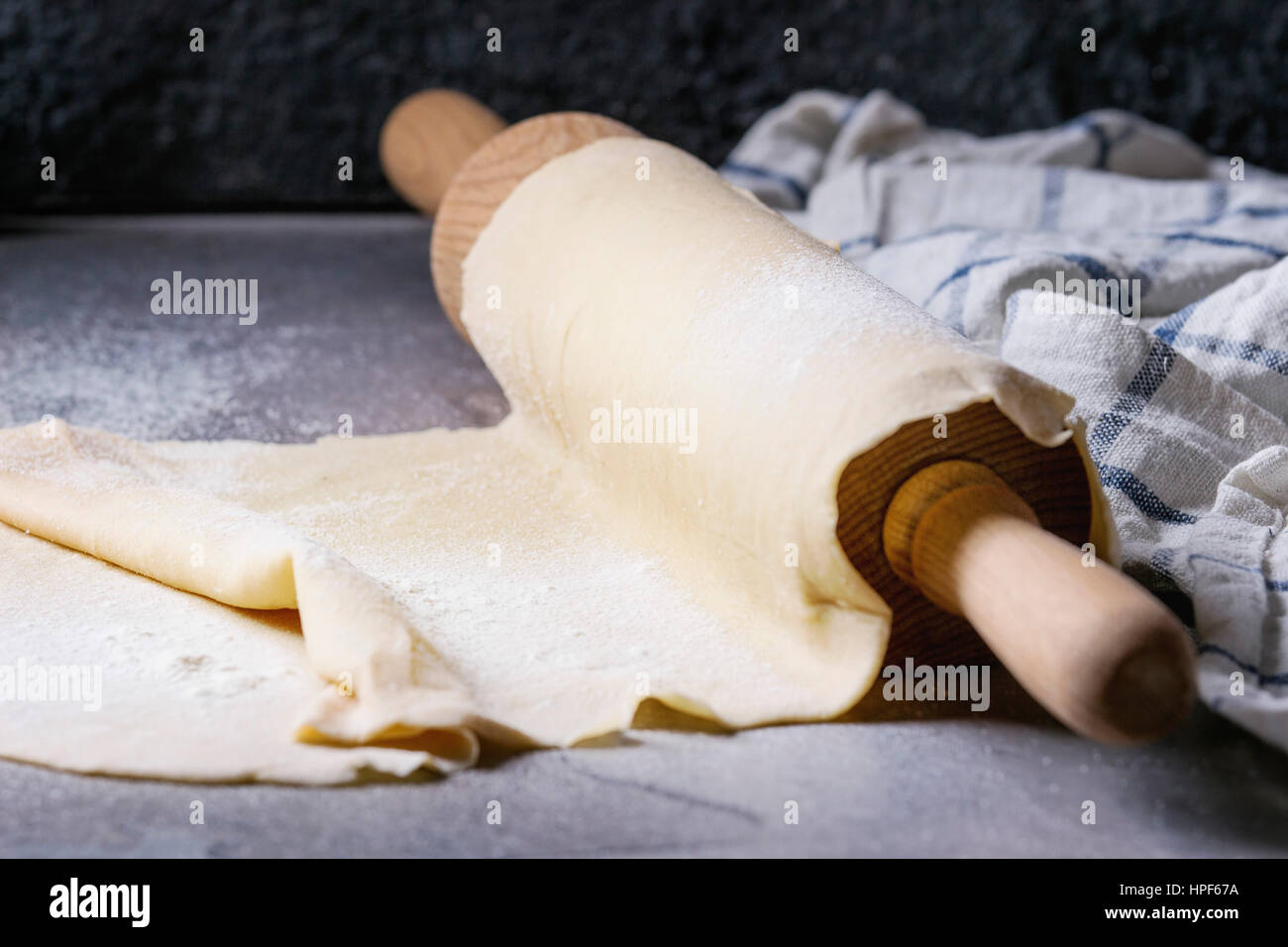 Frische hausgemachte Teig für Nudeln Tagliatelle auf Holz Nudelholz mit Küchentuch über dunklen grauen Tabellenhintergrund gerollt. Stockfoto