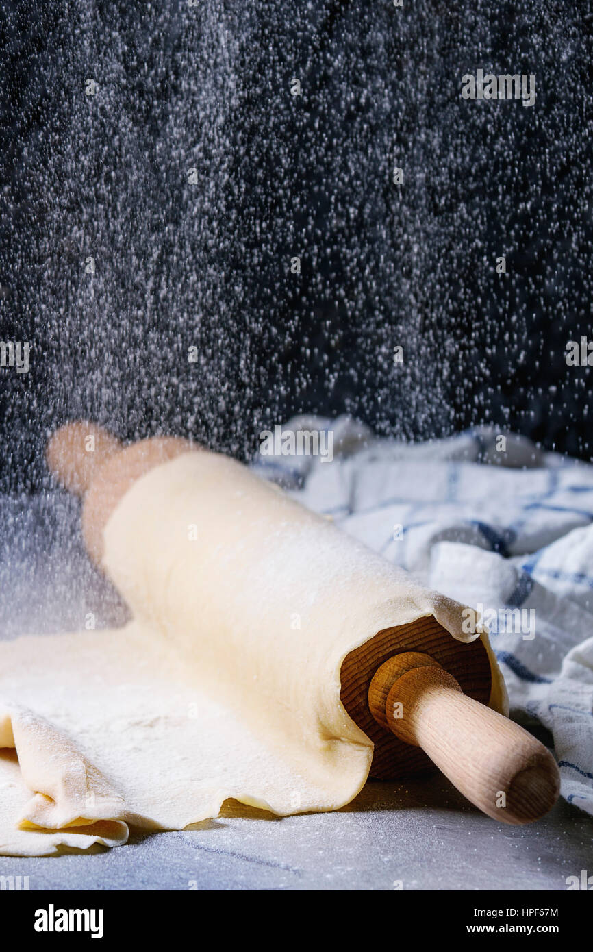 Frische hausgemachte Teig für Nudeln Tagliatelle auf Holz Nudelholz mit Sieb Prise Mehl und Küche Handtuch über dunklen grauen Tabellenhintergrund gerollt. Stockfoto