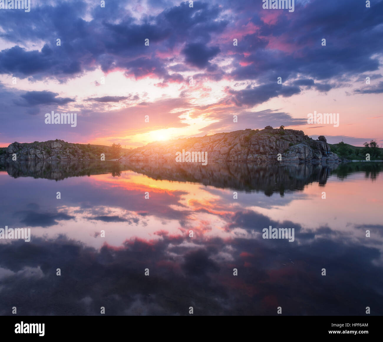 Fluss gegen bunten Himmel mit Wolken und Felsen bei Sonnenuntergang im Sommer. Wunderschöne Landschaft mit See, Berge, Sonne und blauen Wolkenhimmel Stockfoto