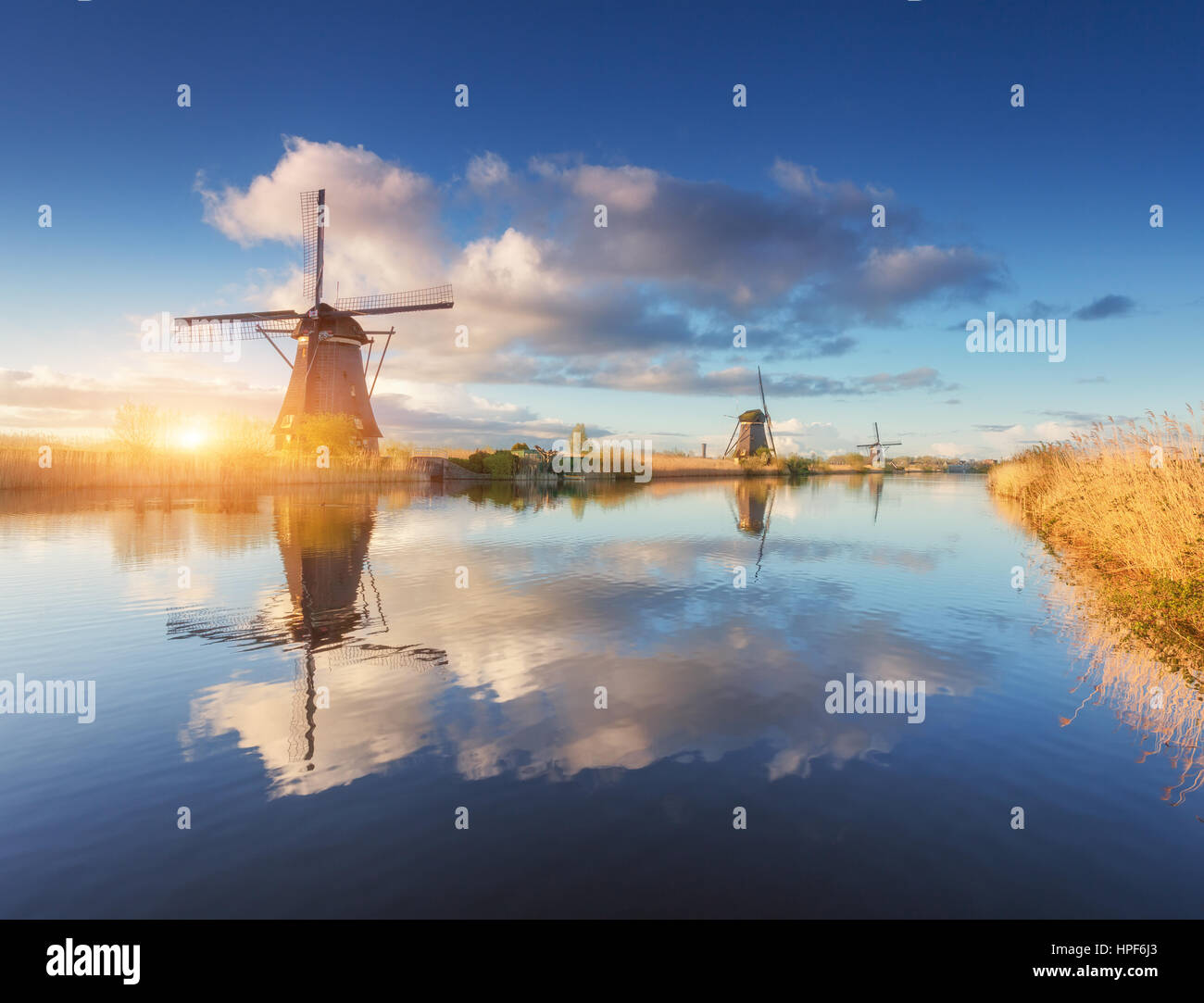 Windmühlen bei Sonnenaufgang. Rustikale Landschaft mit erstaunlichen holländische Windmühlen in der Nähe der Wasserkanäle mit blauen Himmel und Wolken spiegeln sich in Wasser Stockfoto