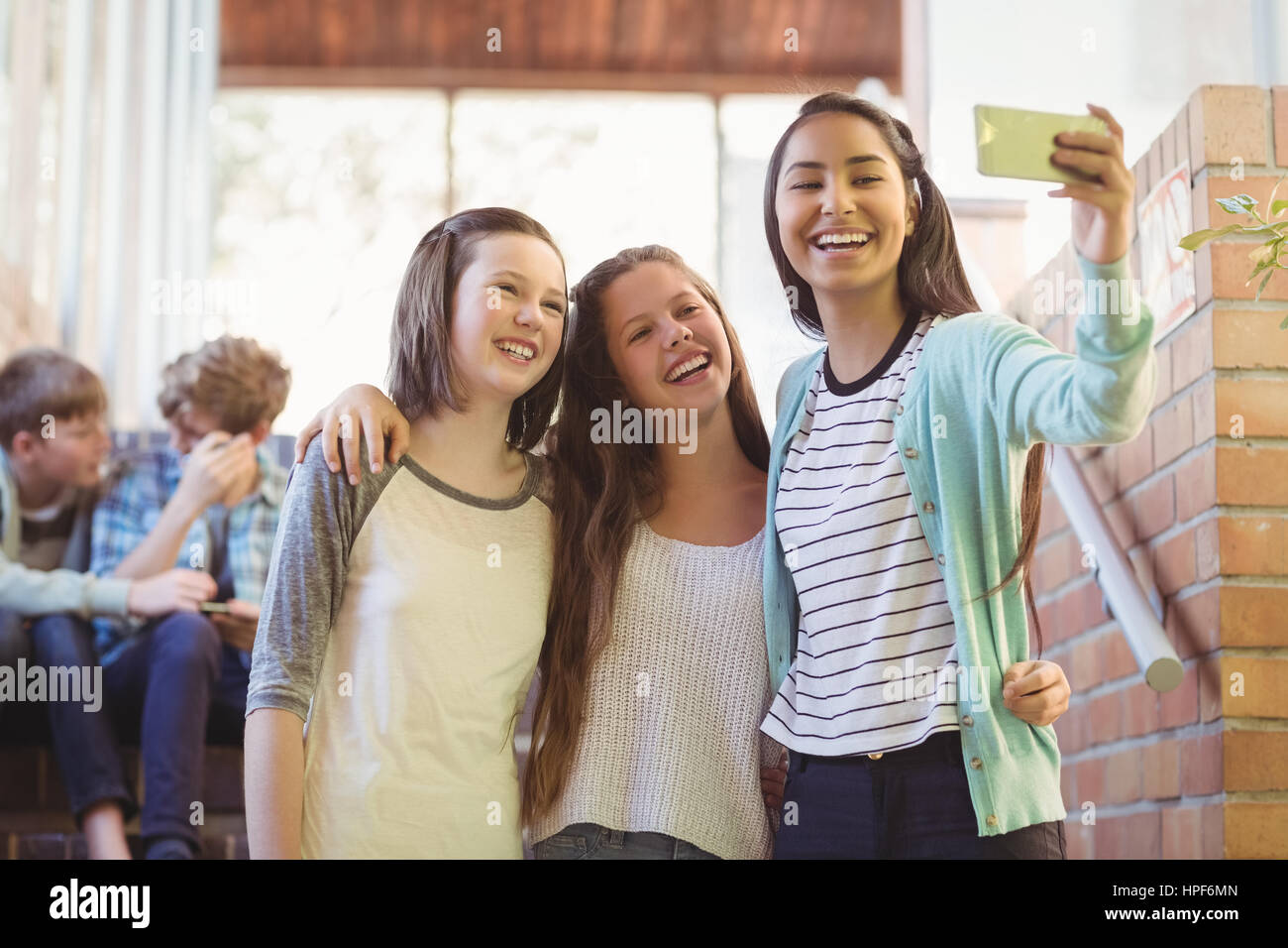 Lächelnd Schülerinnen nehmen Selfie mit Handy im Korridor in der Schule Stockfoto