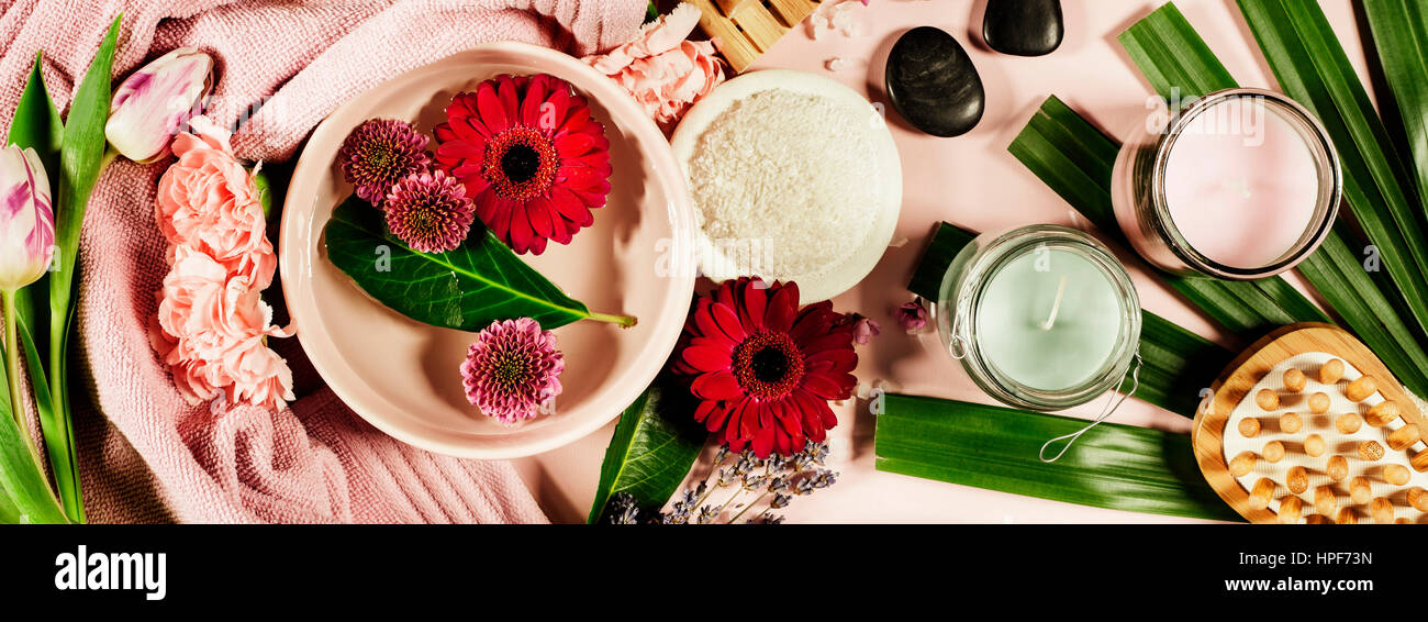 Spa-Hintergrund mit Meersalz, Schüssel, Blumen, Wasser, Seife, Kerzen, ätherische Öle, massage-Bürste und Blumen, Ansicht von oben. Flach zu legen. Rosa Hintergrund Stockfoto