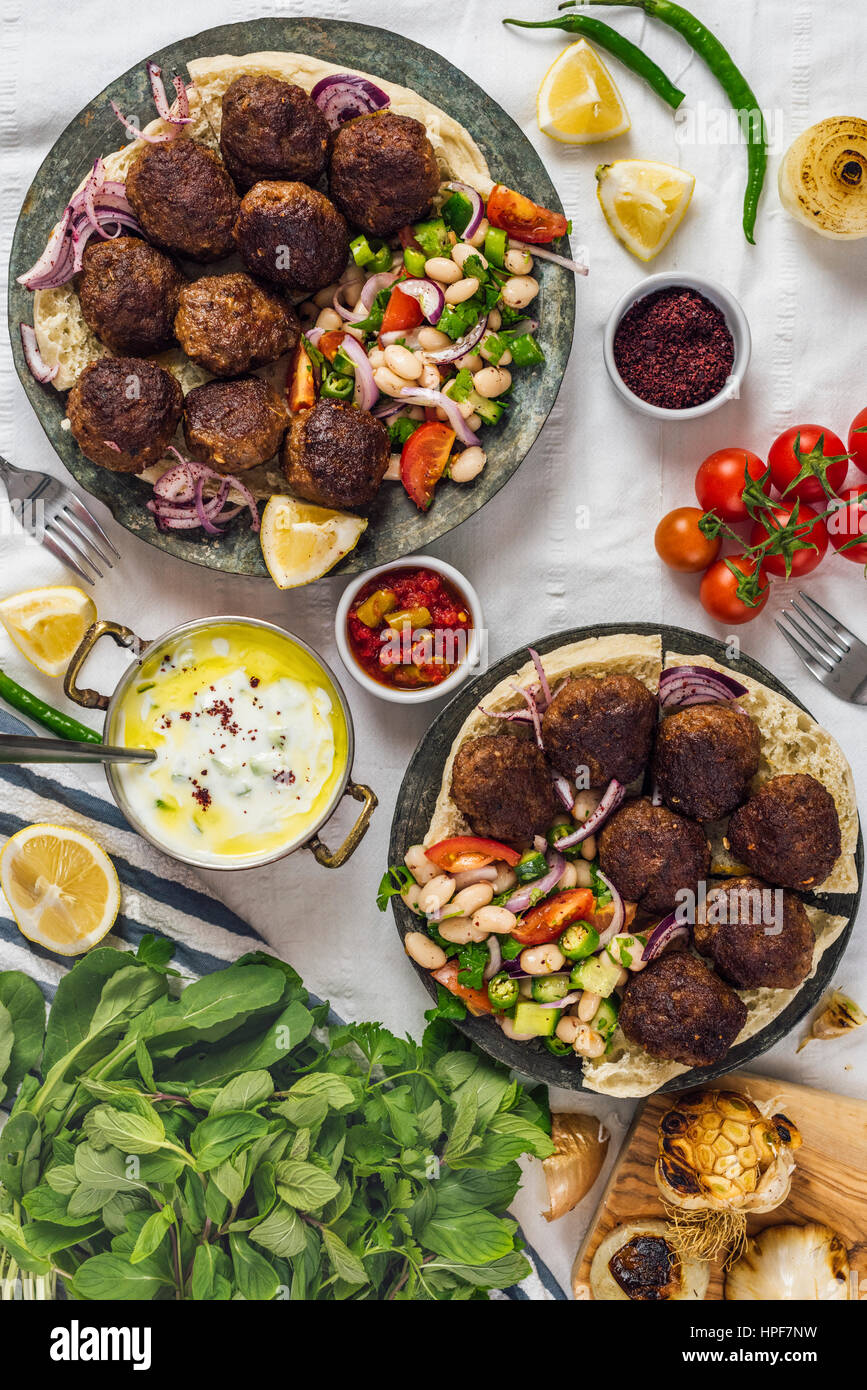 Türkische Frikadellen serviert aka Koftes auf Pita-Brot auf zwei Kupferplatten mit kalten Bohnensalat und roten Zwiebeln aus Draufsicht fotografiert. Joghurt-Sauce, h Stockfoto