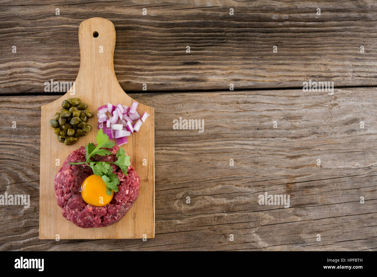 Hackfleisch mit Eigelb, Zwiebeln und Oliven auf Holztablett aus Holz Hintergrund Stockfoto