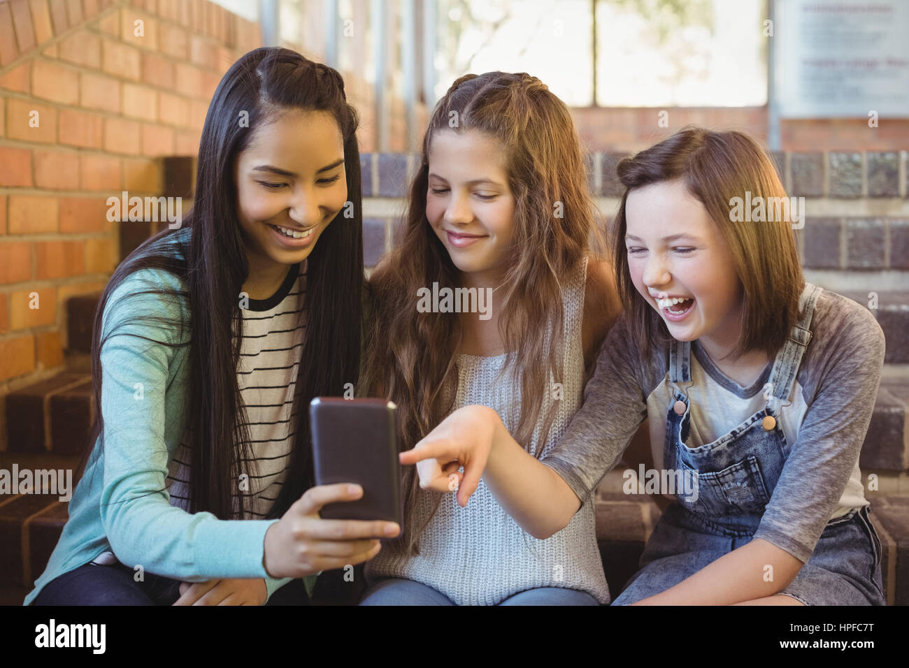 Schulmädchen auf der Treppe mit Handy in der Schule sitzt lächelnd Stockfoto