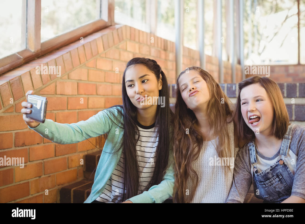 Schulmädchen auf der Treppe nehmen Selfie mit Handy in der Schule sitzt lächelnd Stockfoto