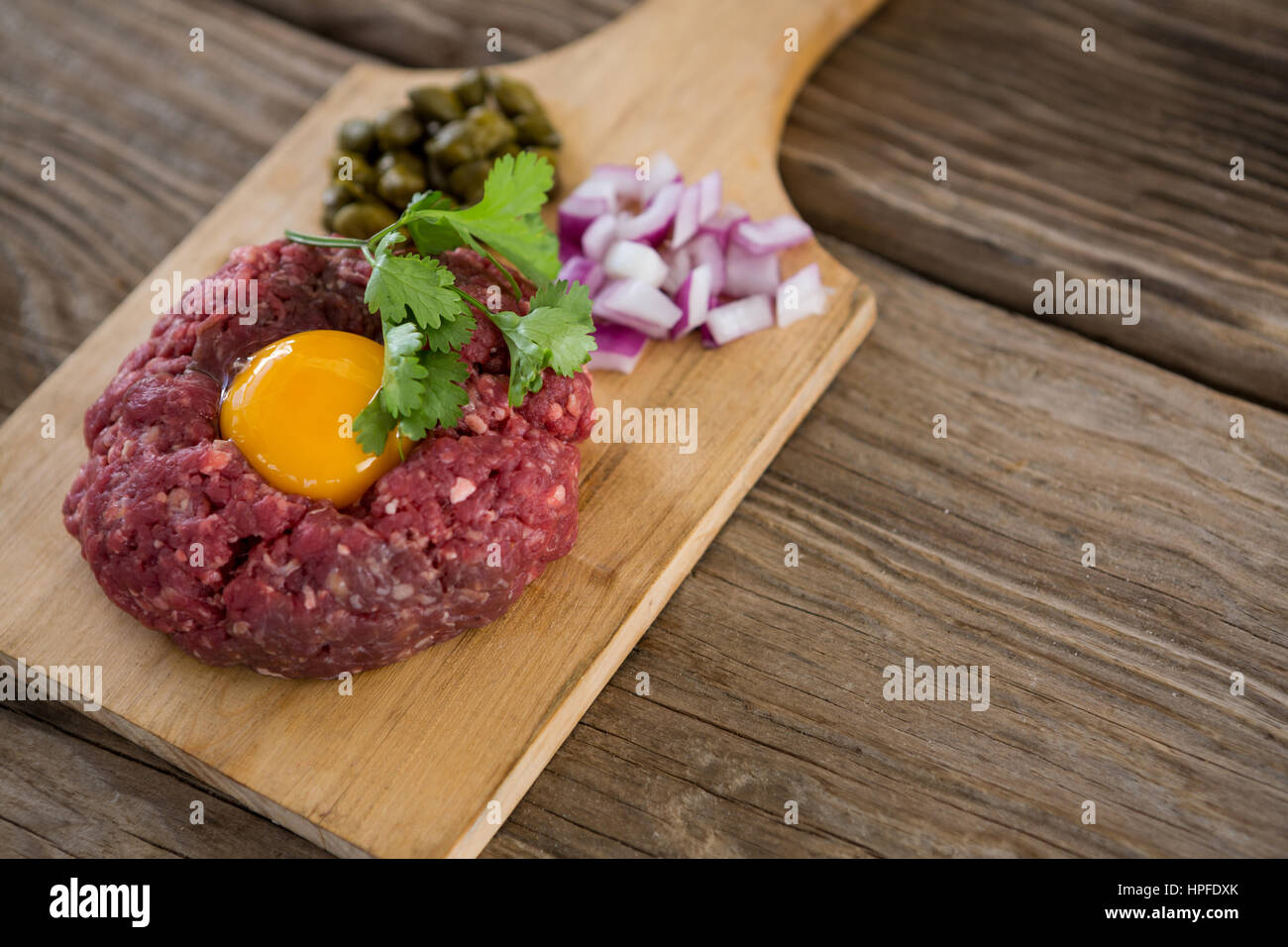 Hackfleisch mit Eigelb, Zwiebeln und Oliven auf Holztablett aus Holz Hintergrund Stockfoto