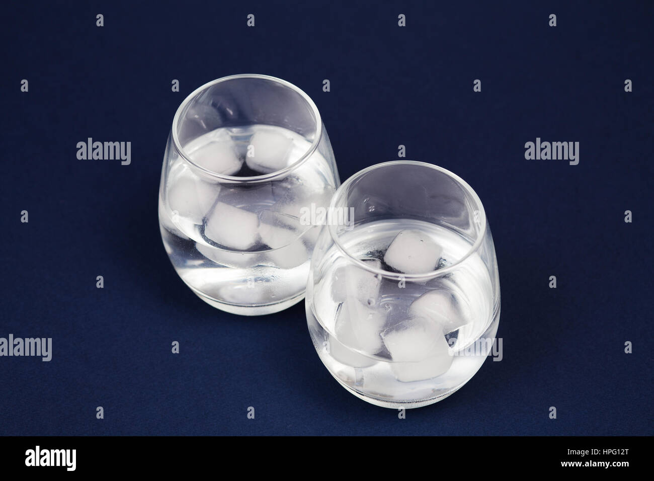 Gläser mit Wasser und Eis isoliert auf dunkelblau Stockfoto