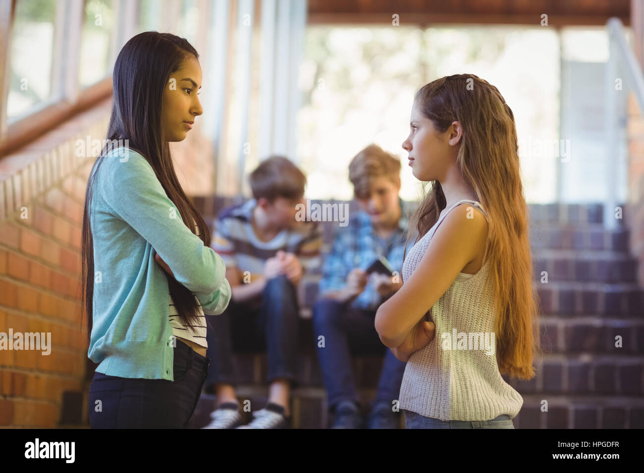 Zwei Schulmädchen mit Arme gekreuzt von Angesicht zu Angesicht stehen im Flur in der Schule Stockfoto