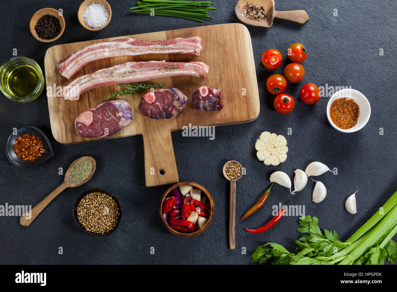 Sorten von Fleisch mit Gewürzen auf Holzbrett vor schwarzem Hintergrund Stockfoto