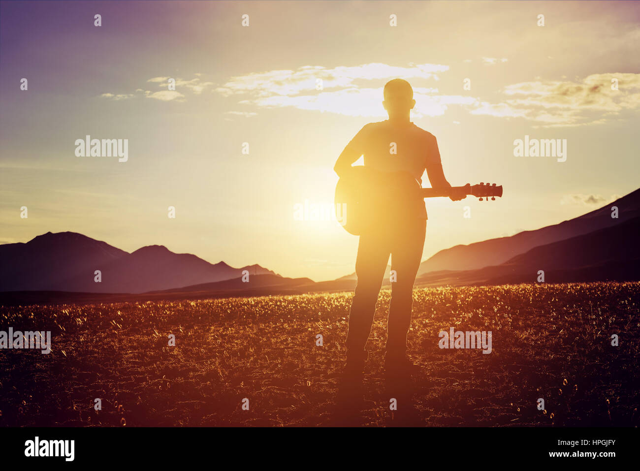 Der Mensch steht mit Gitarre bei Sonnenuntergang und die Berge Bacgdrop. Musik Reisekonzept Stockfoto