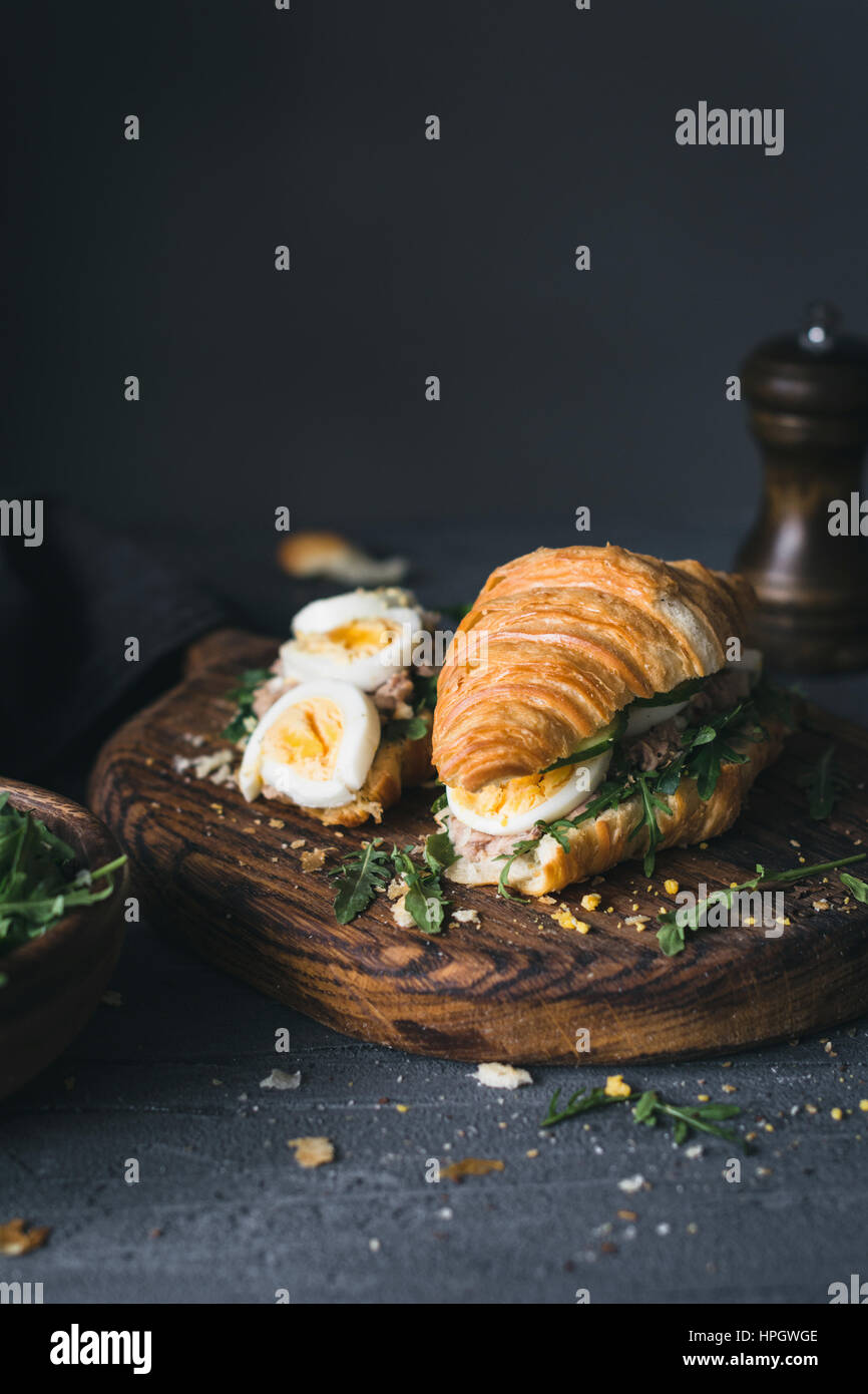 Croissant-Thunfisch-Sandwich mit gekochtem Ei, Rucola, Gurken und Thunfisch Salat auf Holzbrett. Nahaufnahme, selektiven Fokus Stockfoto