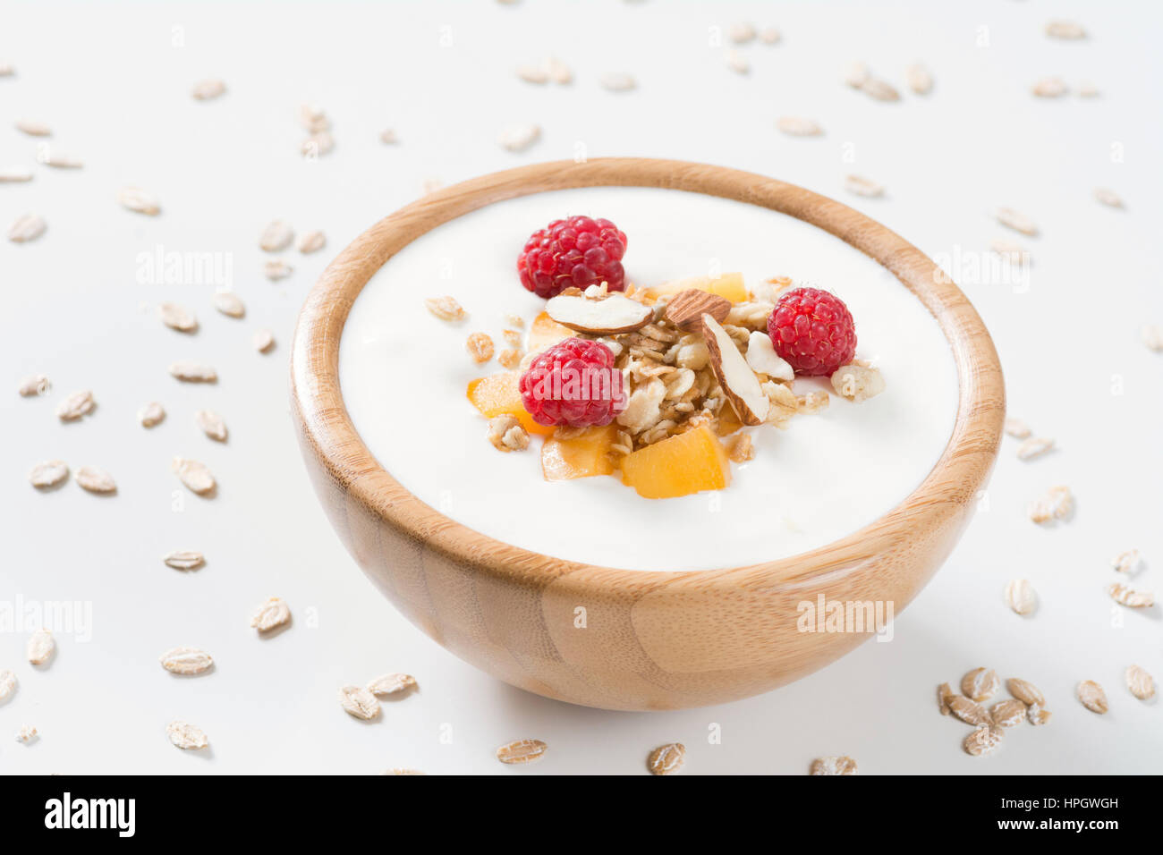 Joghurt Schüssel mit frischen Himbeeren, Aprikosen und Müsli in einer Holzschale auf weißem Hintergrund. Essen für gesundes Frühstück, Ernährung und gesundes Leben Stockfoto