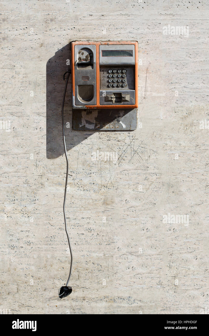 Vertikale Vorderansicht des beschädigten orange öffentliches Telefon mit gebrochenen Hörer gegen eine verkratzte weiße Wand hängenden Stockfoto