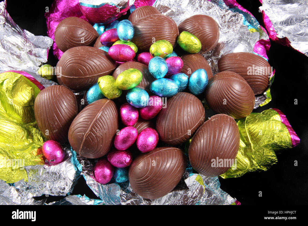 Haufen von unverpackten Schokoladeneier mit bunter Folie wickeln rund um es auf einem schwarzen Hintergrund. Stockfoto