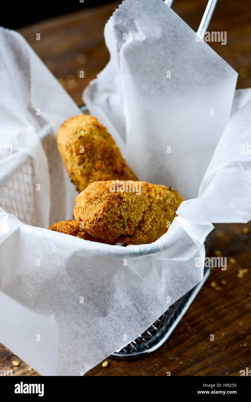 einige hausgemachte Croquetas, spanische Kroketten, serviert in einem Metallkorb, platziert auf einem rustikalen Holztisch Stockfoto