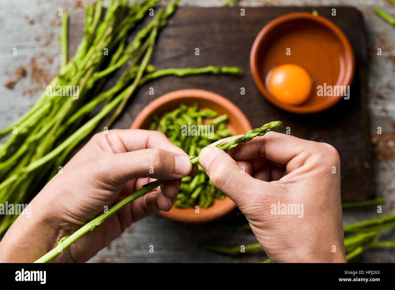 junger Mann hacken wilder Spargel mit seinen Händen und einige Steingut Schüsseln mit geschnittenen Spargel und einer gerissenen Ei Zutaten, um eine möglichst vorbereiten Stockfoto