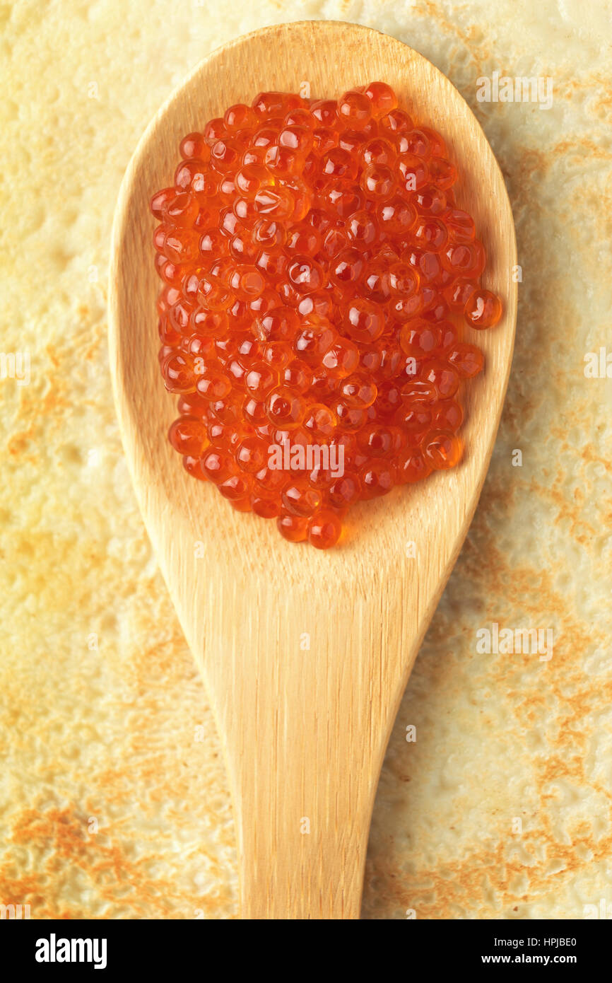 Roter Kaviar auf Holzlöffel auf Pfannkuchen Hintergrund. Russische Delikatesse. Traditionelles Essen für Masleniza Stockfoto