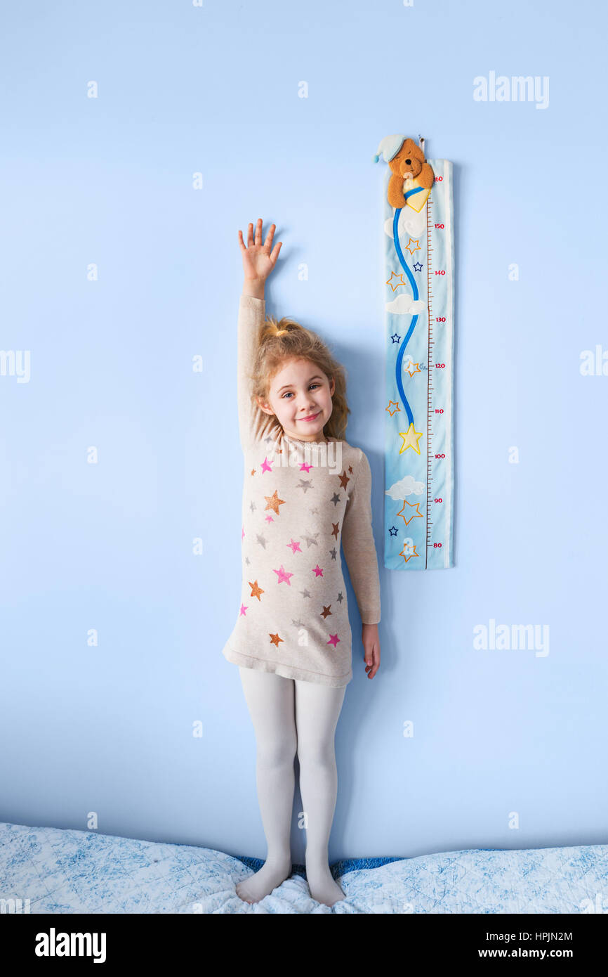 Kleine blonde Mädchen, die Messung der Höhe gegen die Wand im Zimmer Stockfoto