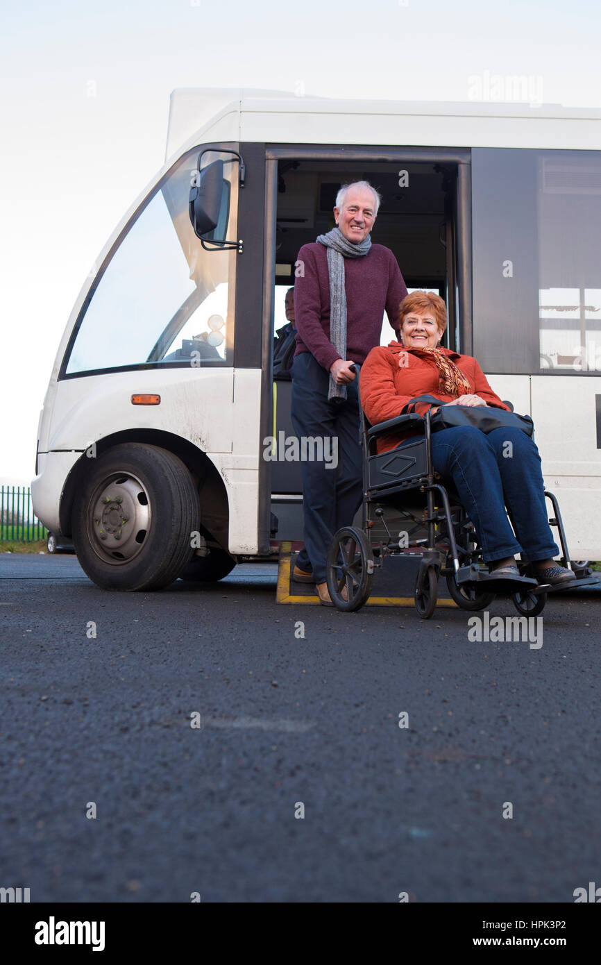 Älteres Ehepaar Lächeln für die Kamera, als sie aus dem Bus steigen. Der Mann schiebt seinen Rollstuhl gefesselten Frau. Stockfoto