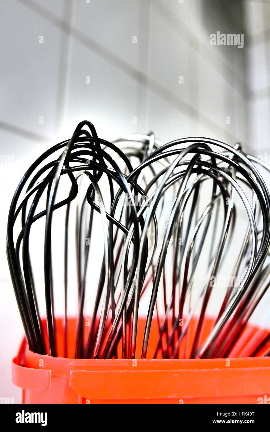 Metall Essen Rührbesen in roten Kunststoff-Container Hintergrund weiß geflieste Küche Stockfoto