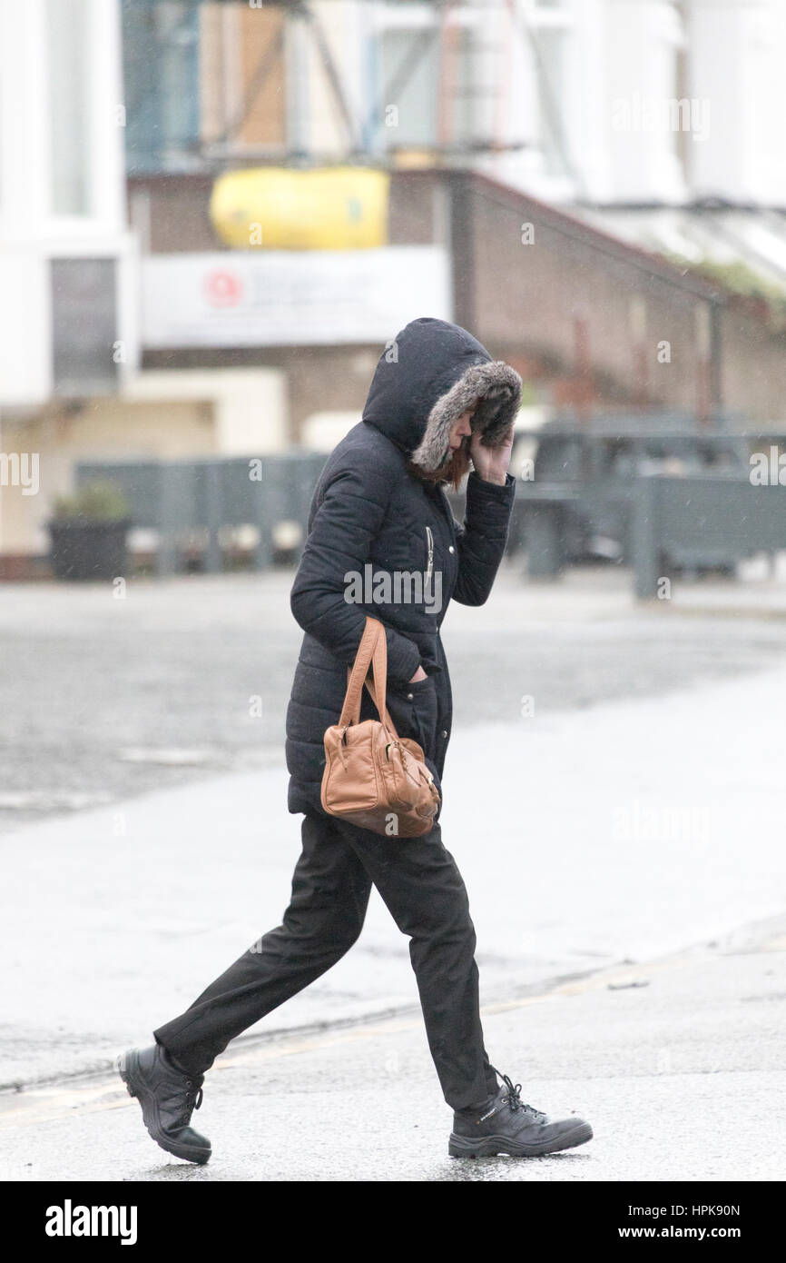 Weibliche Pendler zu Fuß zur Arbeit bei nassen und windigen Wetter infolge Sturm Doris, da traf es Llandudno, Nordwales Stockfoto