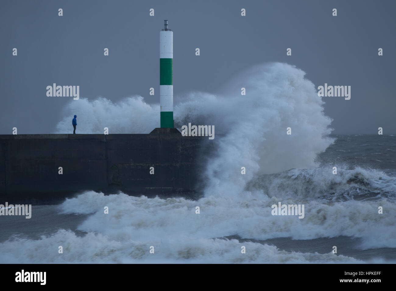 Ein Mann steht auf einem Steg zu riskieren, als die grossen Wellen über ihm während Sturm Doris Stockfoto