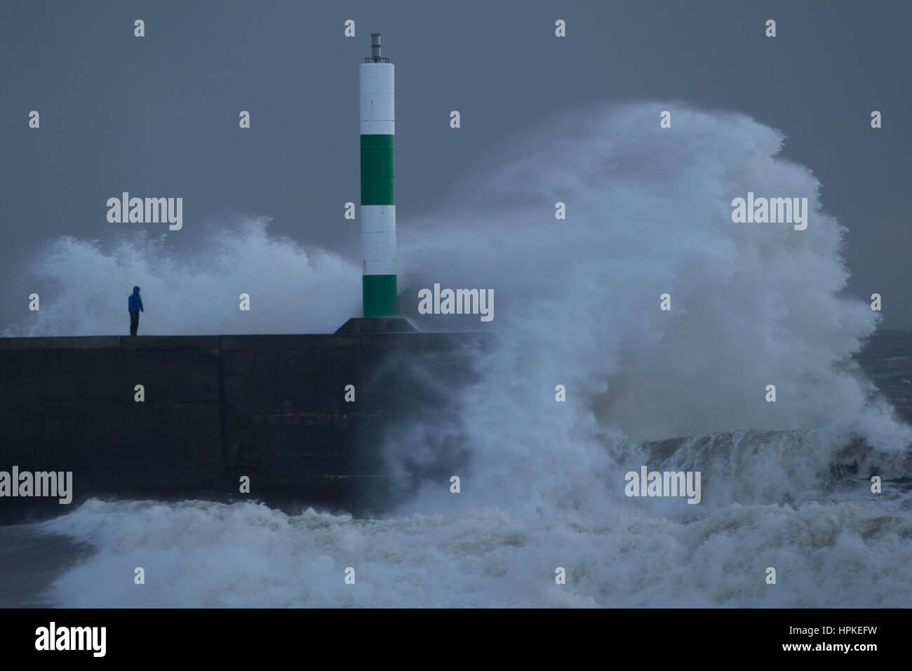 Ein Mann steht auf einem Steg zu riskieren, als die grossen Wellen über ihm während Sturm Doris Stockfoto