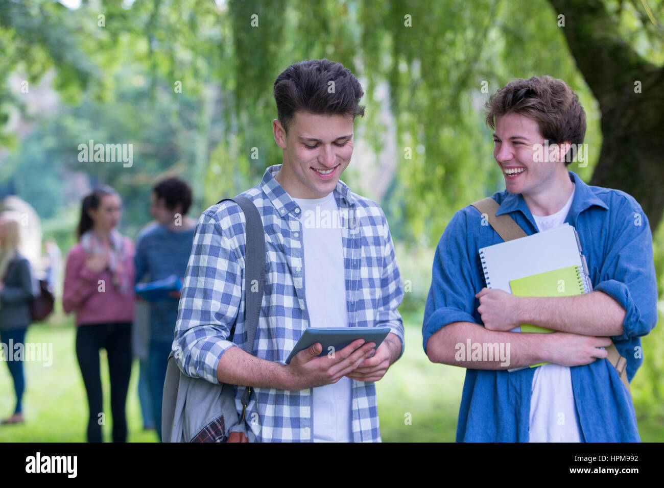 Zwei glückliche männliche Studenten Lächeln, als sie zusammen im Freien zu studieren. Sie verwenden ein digitale Tablet und Bücher. Stockfoto