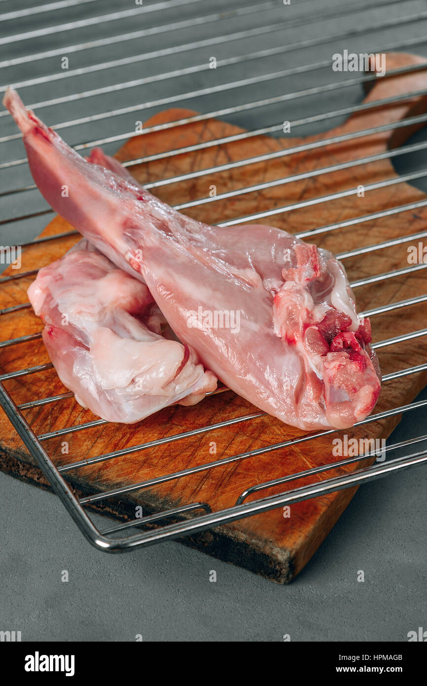 Vorbereitung von Kaninchenfleisch roh. Auf dem Tisch auf einem grauen Hintergrund sind zwei tierische Pfoten. Es entsteht auf der Oberfläche Blut sichtbar Kaninchen Muskel und Knochen. Stockfoto
