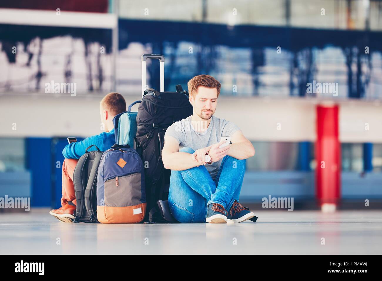 Zwei Freunde, die zusammen reisen. Reisende mit dem Handy am Flughafen Abflugbereich für ihre Verspätung Flug warten. Stockfoto