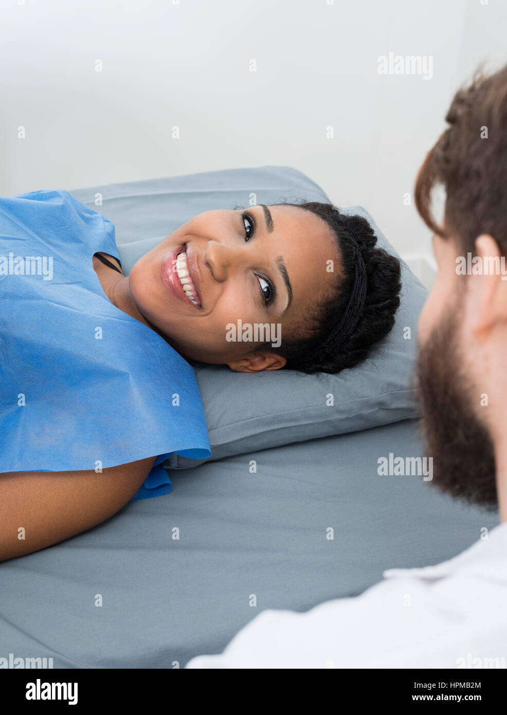 Lächelnde junge Frau betrachten männlichen Arzt beim liegen auf dem Bett in Klinik Stockfoto